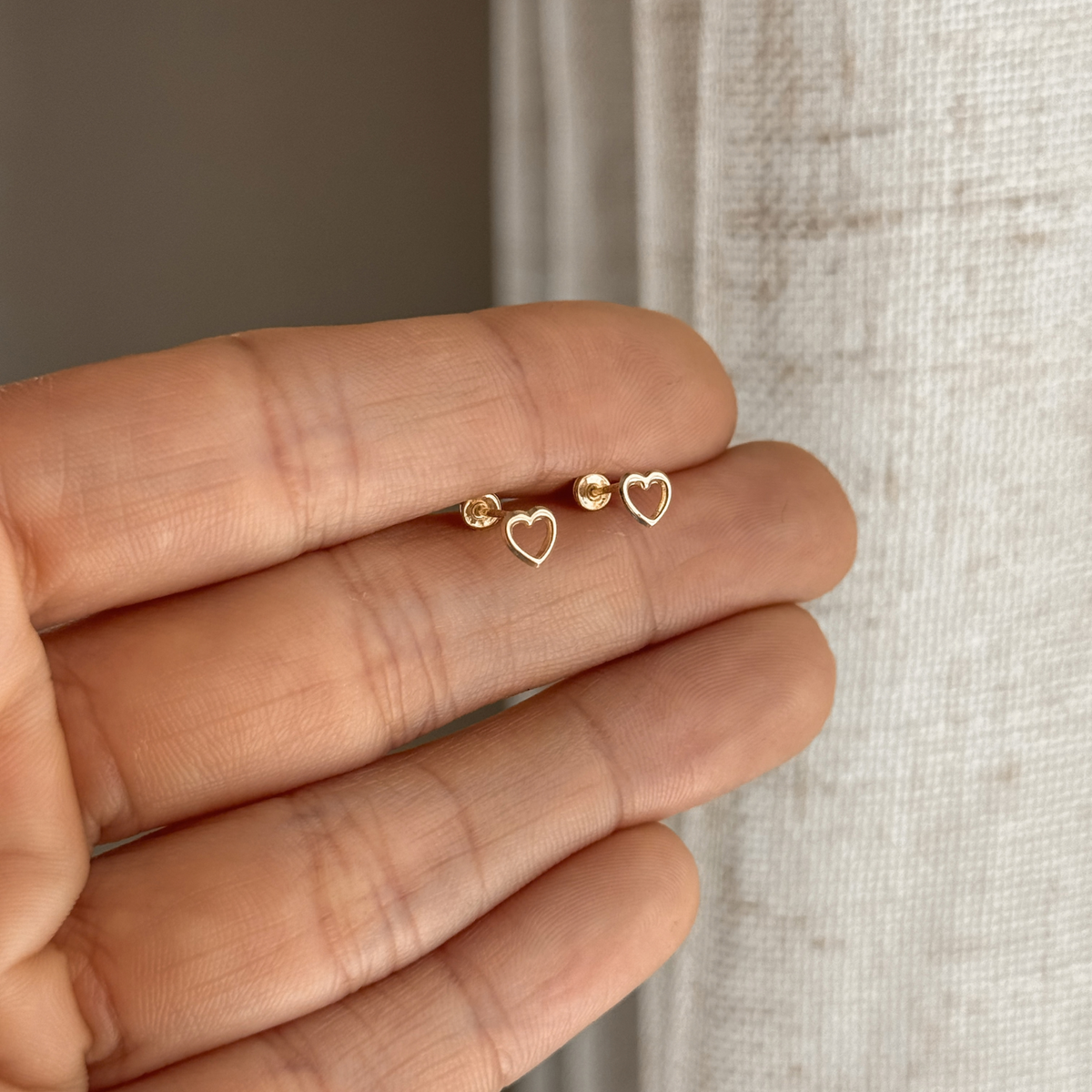 10K solid gold open heart stud earrings held in hand to show their small size – Liv Aura