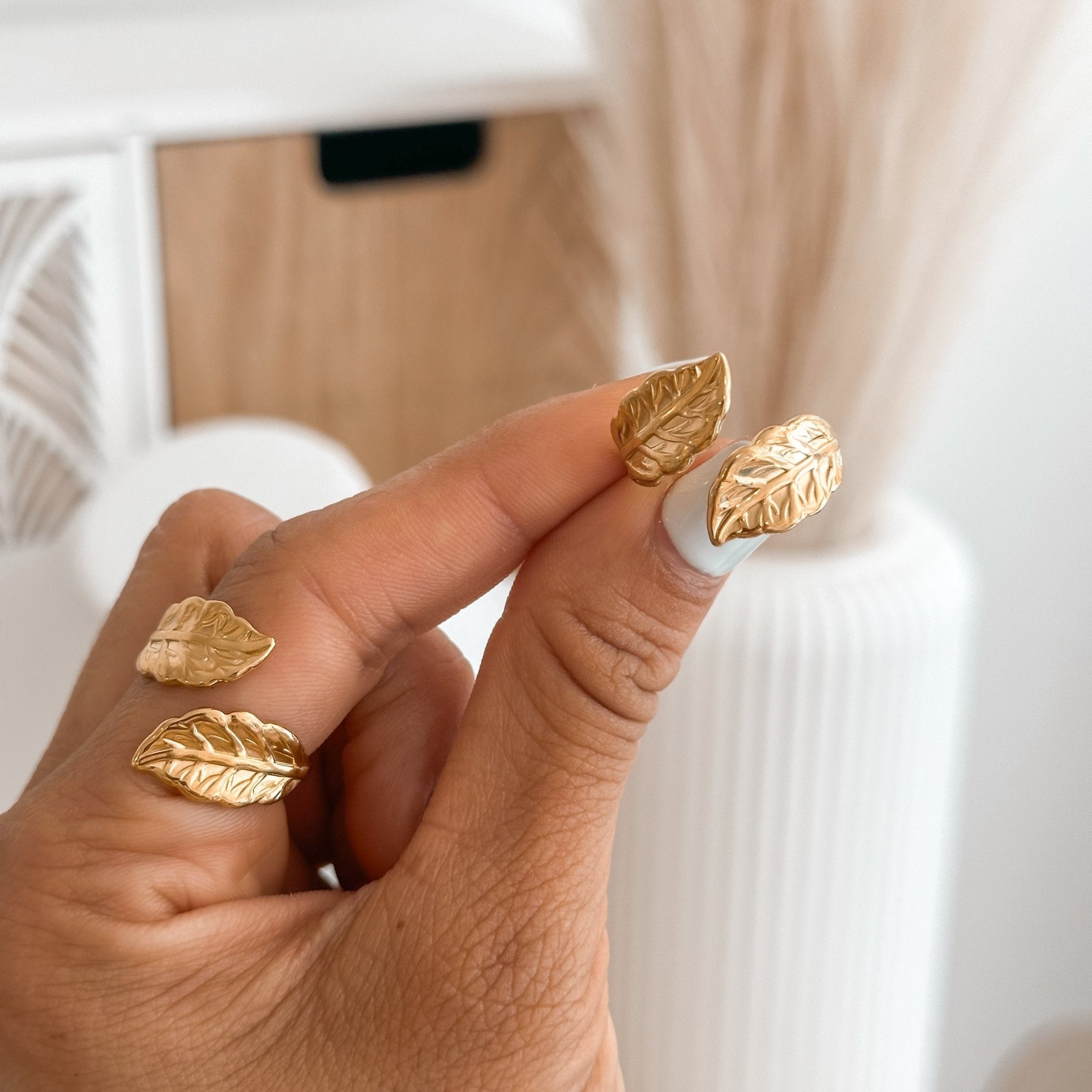Double gold leaf ring held between fingers – textured leaf detail in open adjustable design