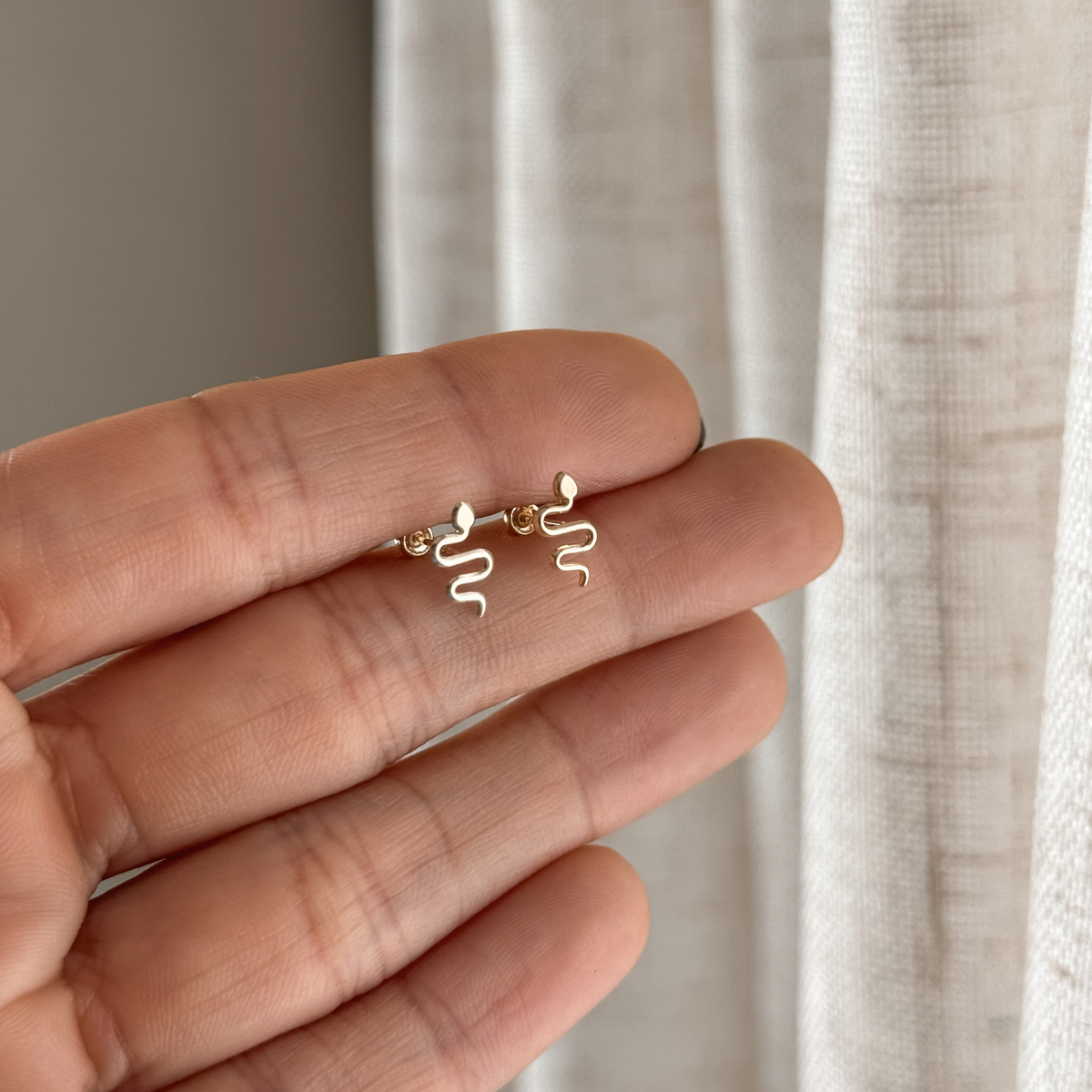 10K solid gold snake stud earrings held in hand to show the size – Liv Aura
