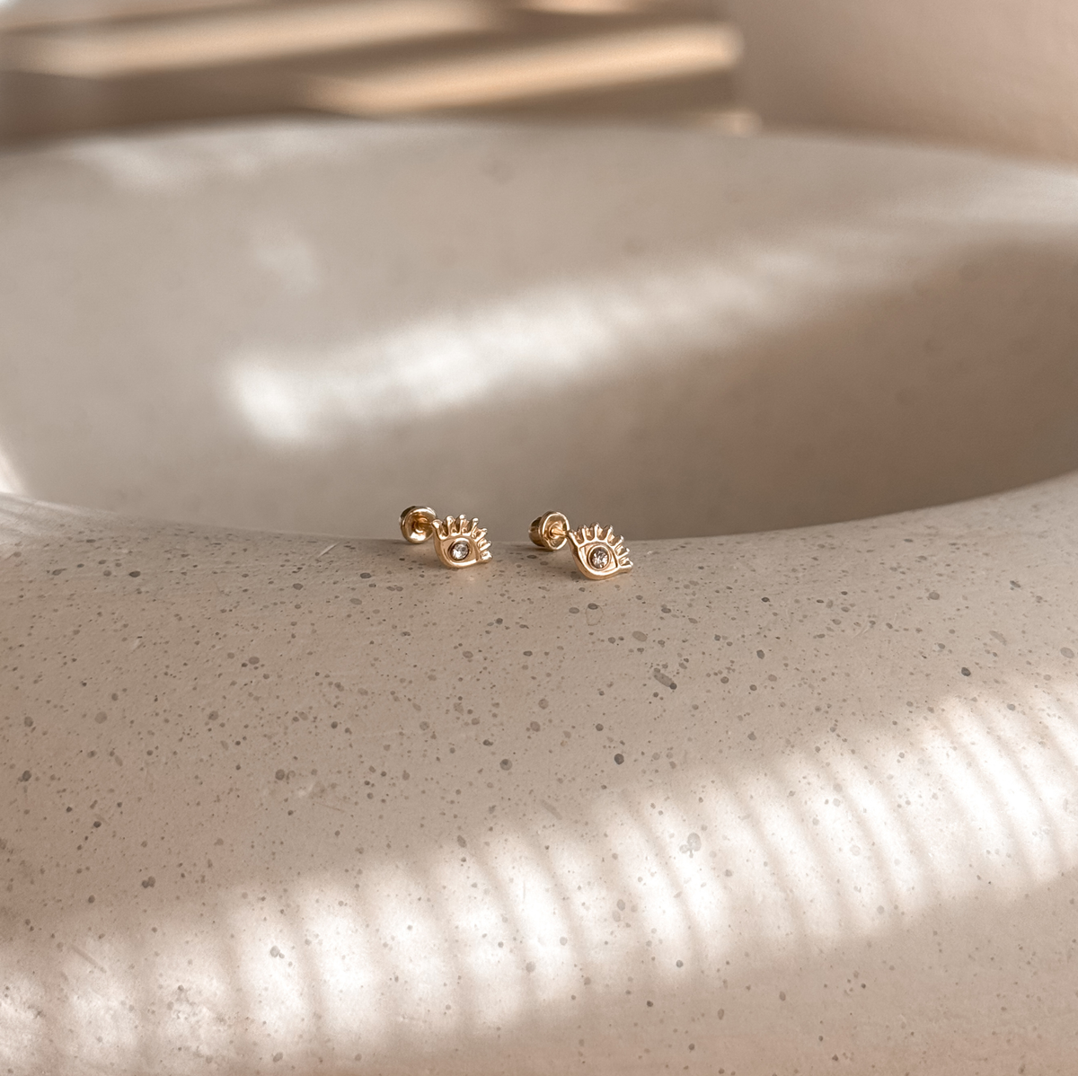 10K solid gold evil eye stud earrings on a speckled stone dish in natural light – Liv Aura