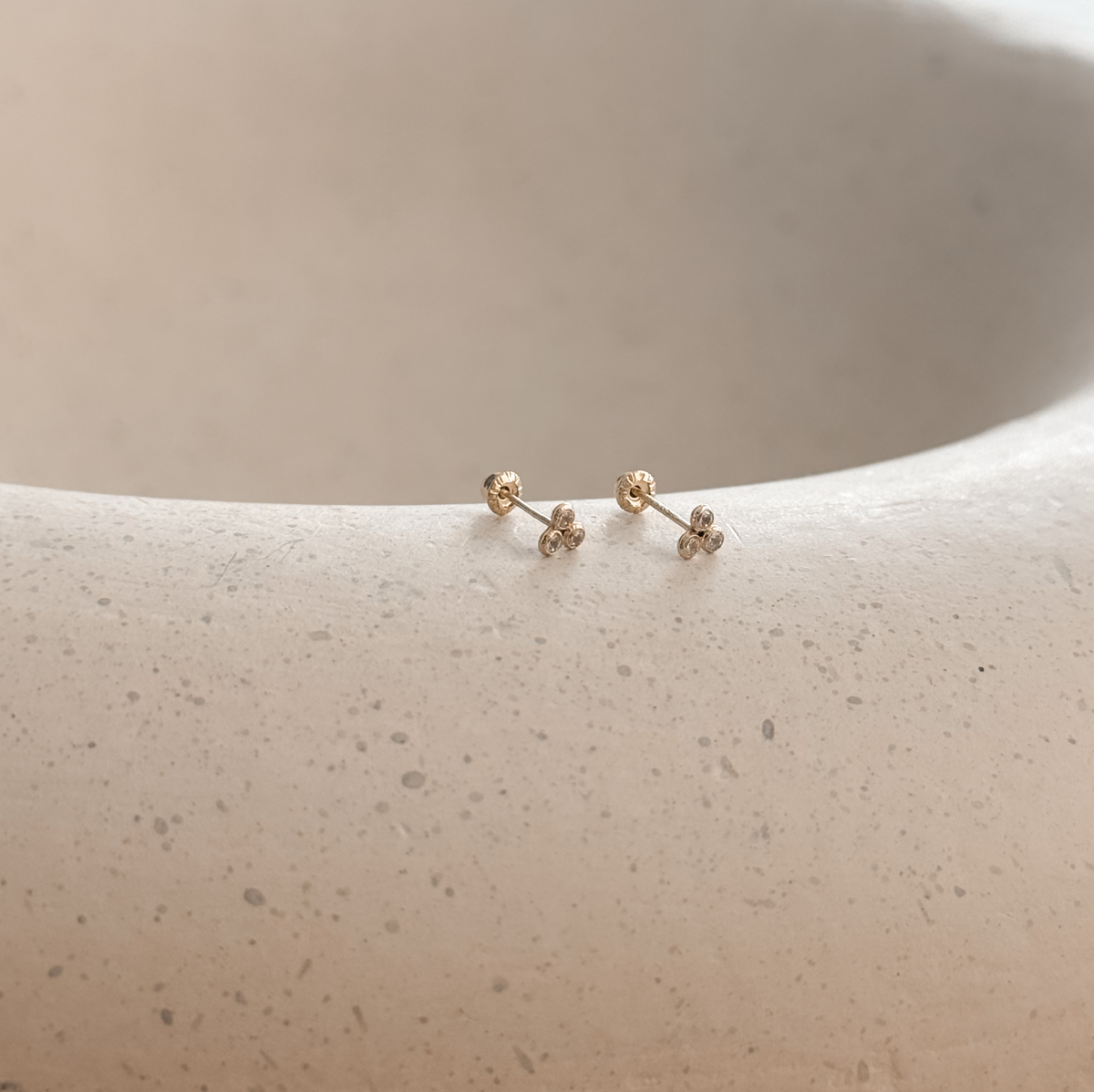 Solid gold CZ trio bezel studs with screw backs on a stone dish, side view – Liv Aura