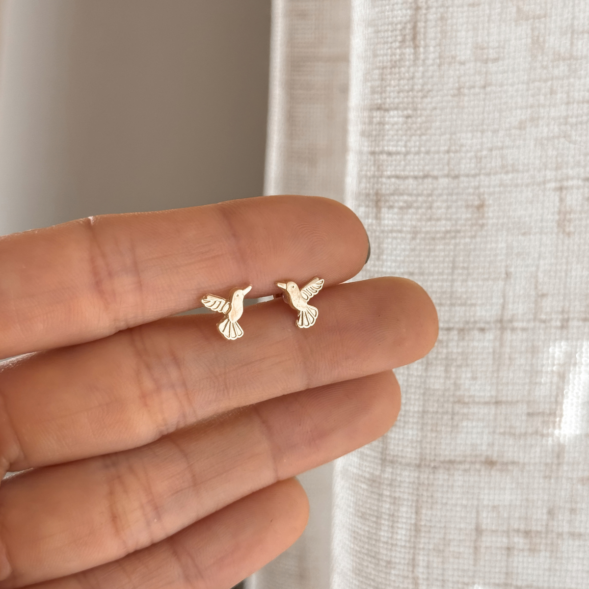 10K solid gold hummingbird stud earrings held in hand to show the size – Liv Aura