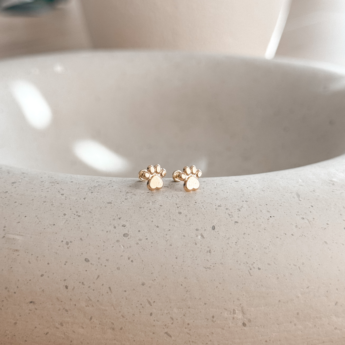 10K solid gold paw print stud earrings on a speckled stone dish – Liv Aura