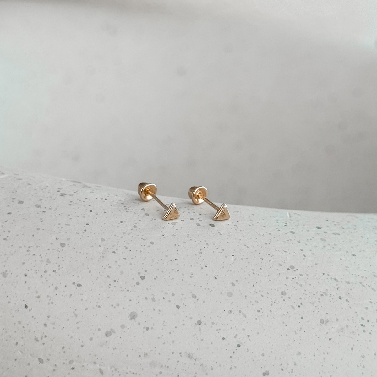 10K solid gold mini triangle stud earrings with screw backs on a speckled stone dish – Liv Aura