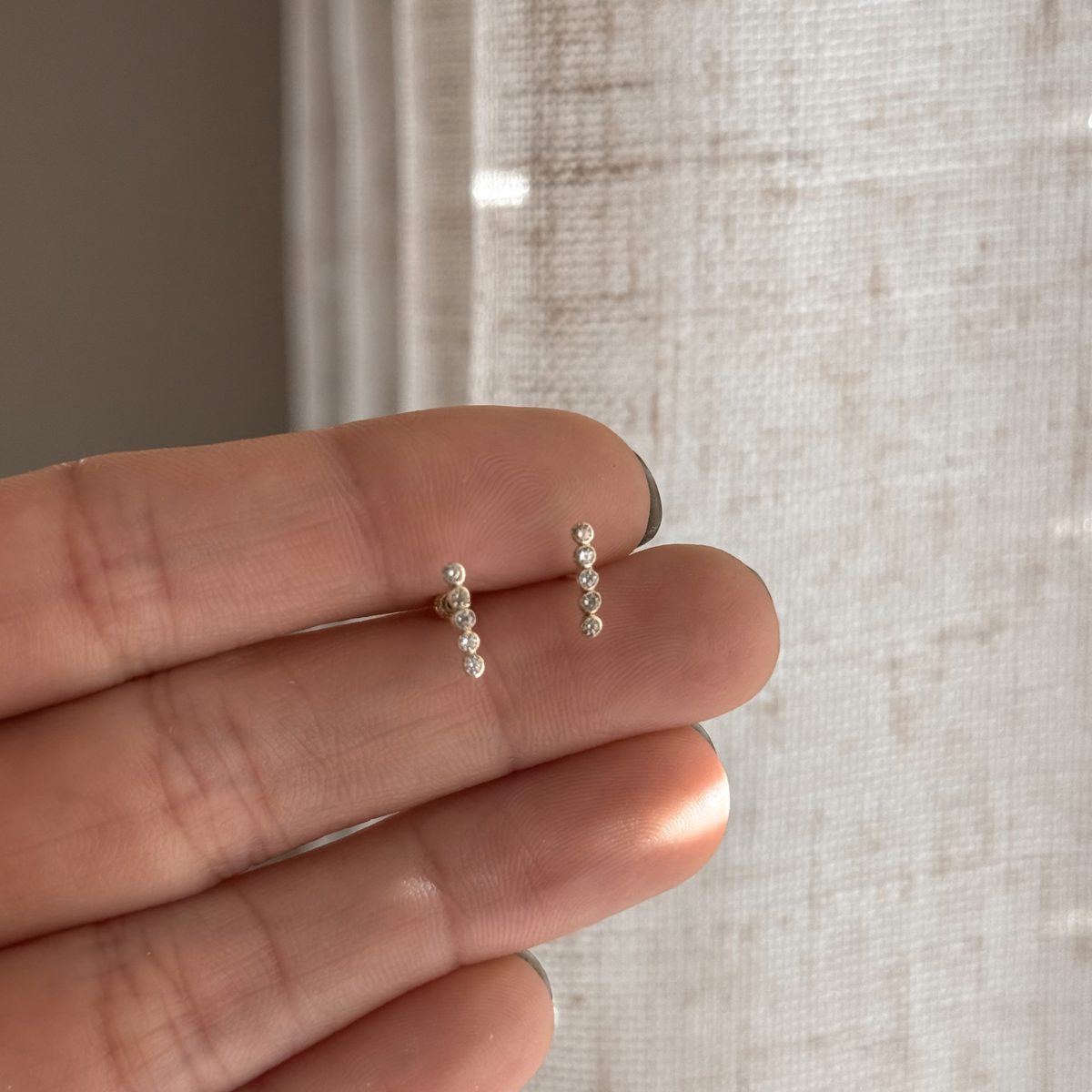 10K solid gold slim CZ bar stud earrings held in hand to show the size – Liv Aura