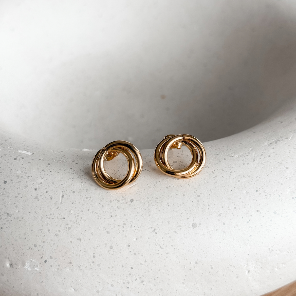 Gold circle stud earrings on a speckled stone dish – Liv Aura