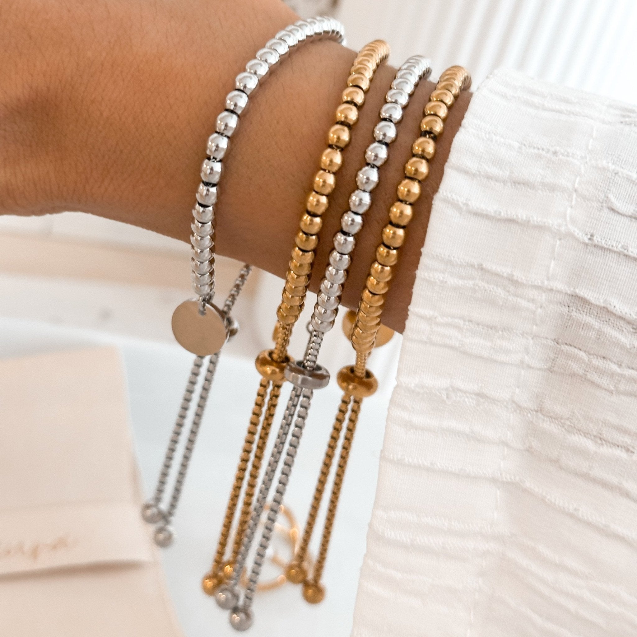 gold and silver bead bracelets shown stacked on wrist with slider