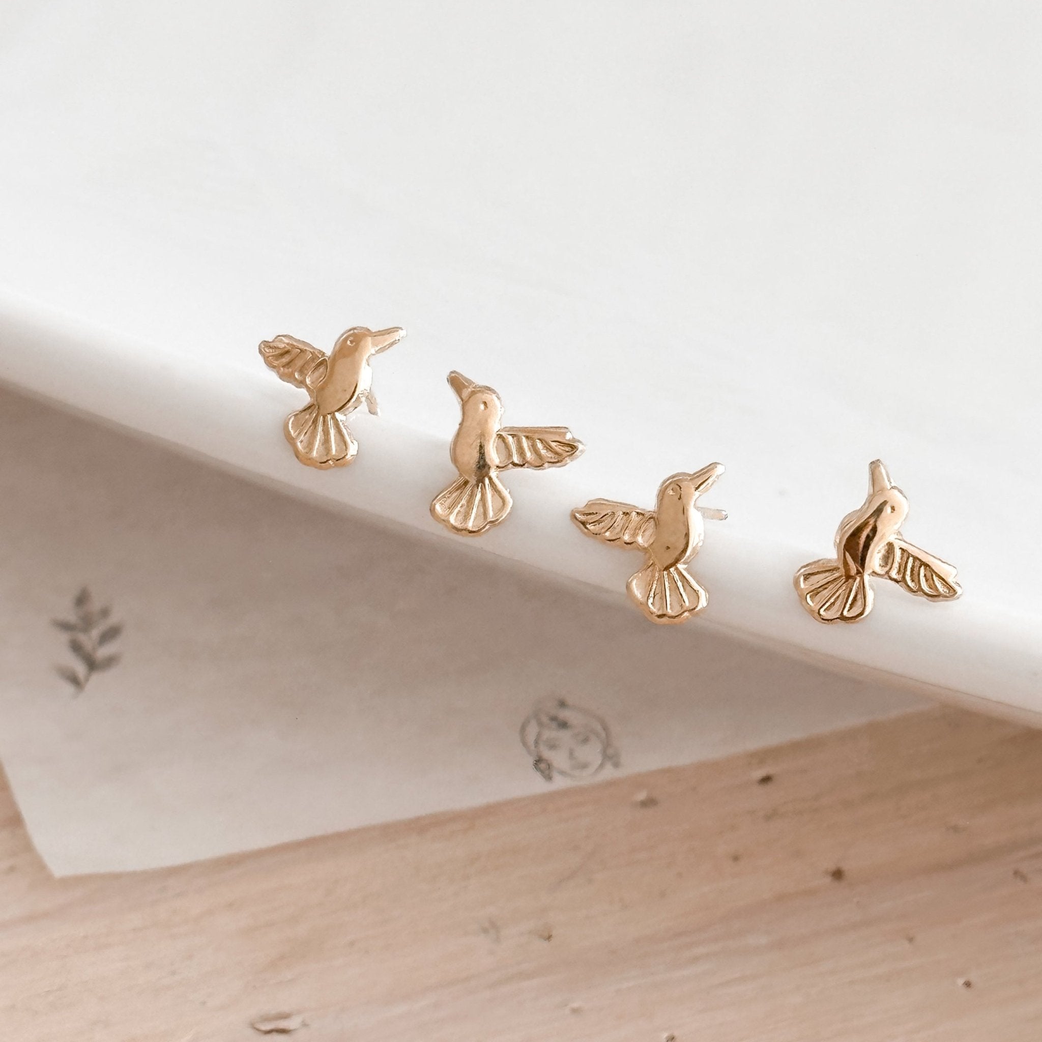 Two 10K gold hummingbird stud earrings displayed on a white ceramic plate, showcasing their delicate bird shape and golden shine.