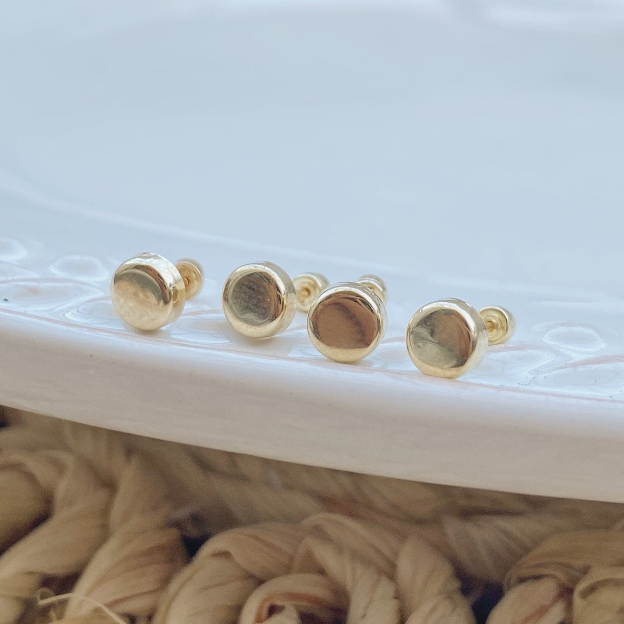 Close-up of dot studs arranged on a white ceramic dish – minimalist 10K gold earrings