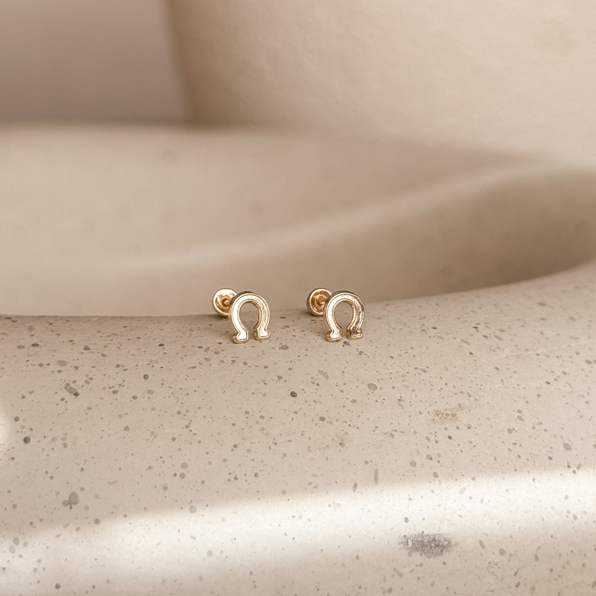 10K solid gold horseshoe stud earrings on a stone dish, side view – Liv Aura
