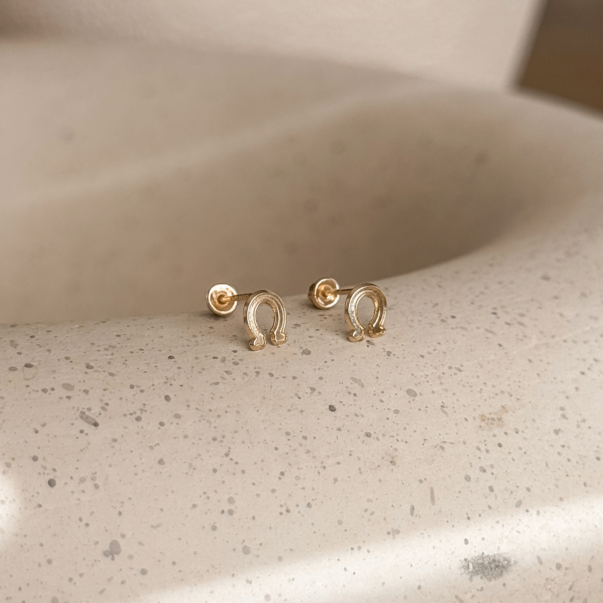 10K solid gold horseshoe stud earrings with screw backs on a speckled stone dish – Liv Aura