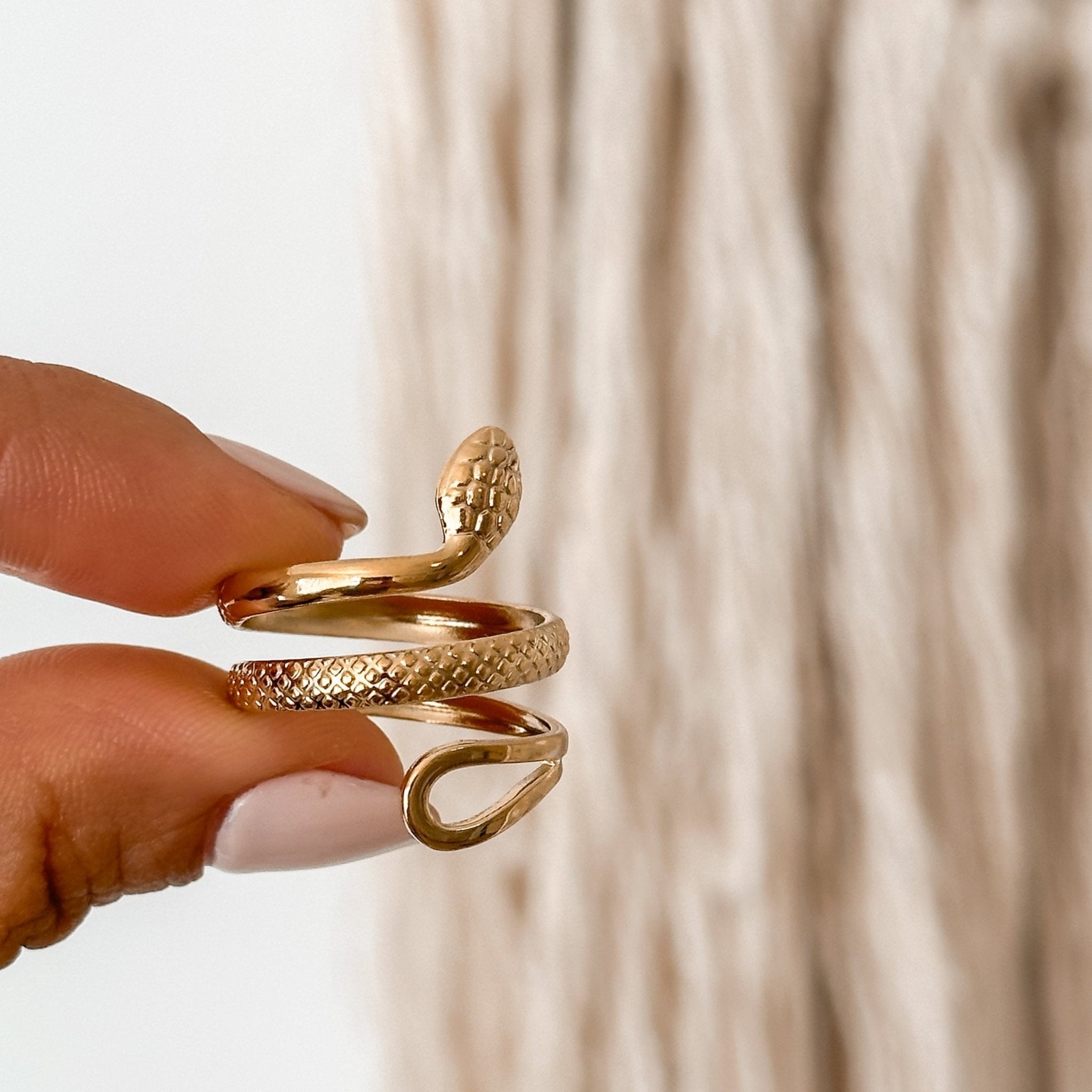 Gold snake ring held gently on fingertip, emphasizing its adjustable band and fine details.
