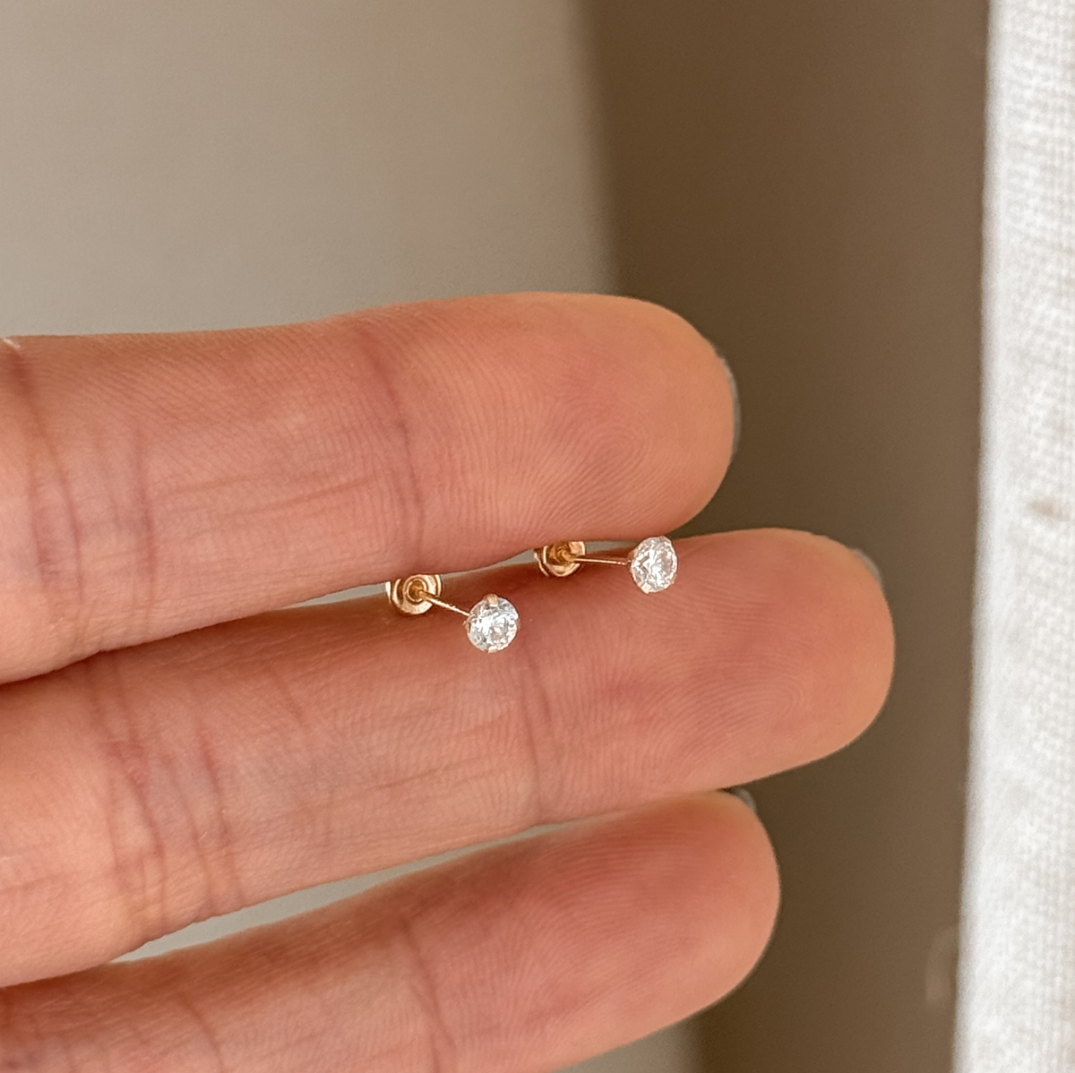 Tiny 3mm CZ solitaire solid gold studs held in hand to show the size – Liv Aura