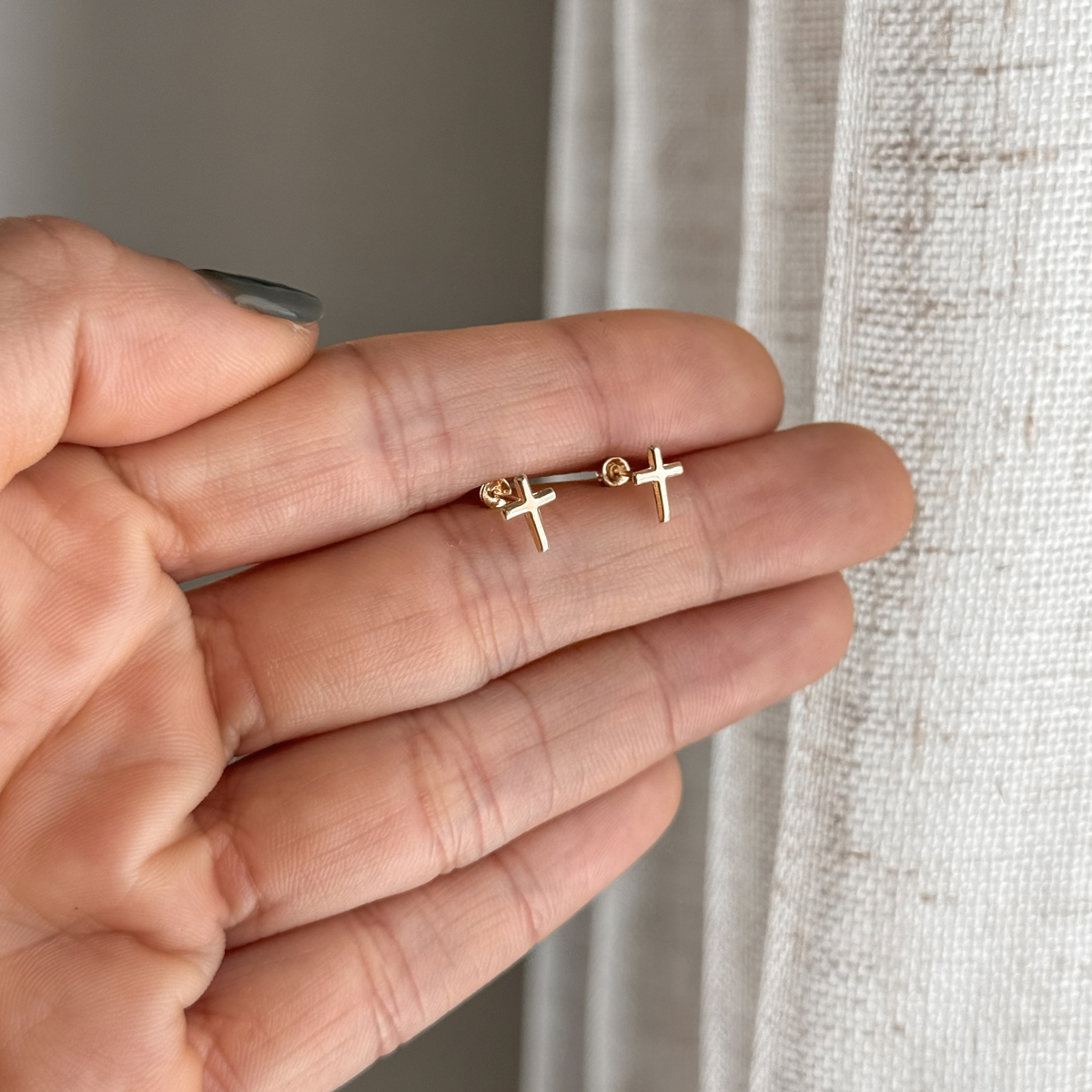 10K solid gold cross stud earrings held in hand to show the size – Liv Aura