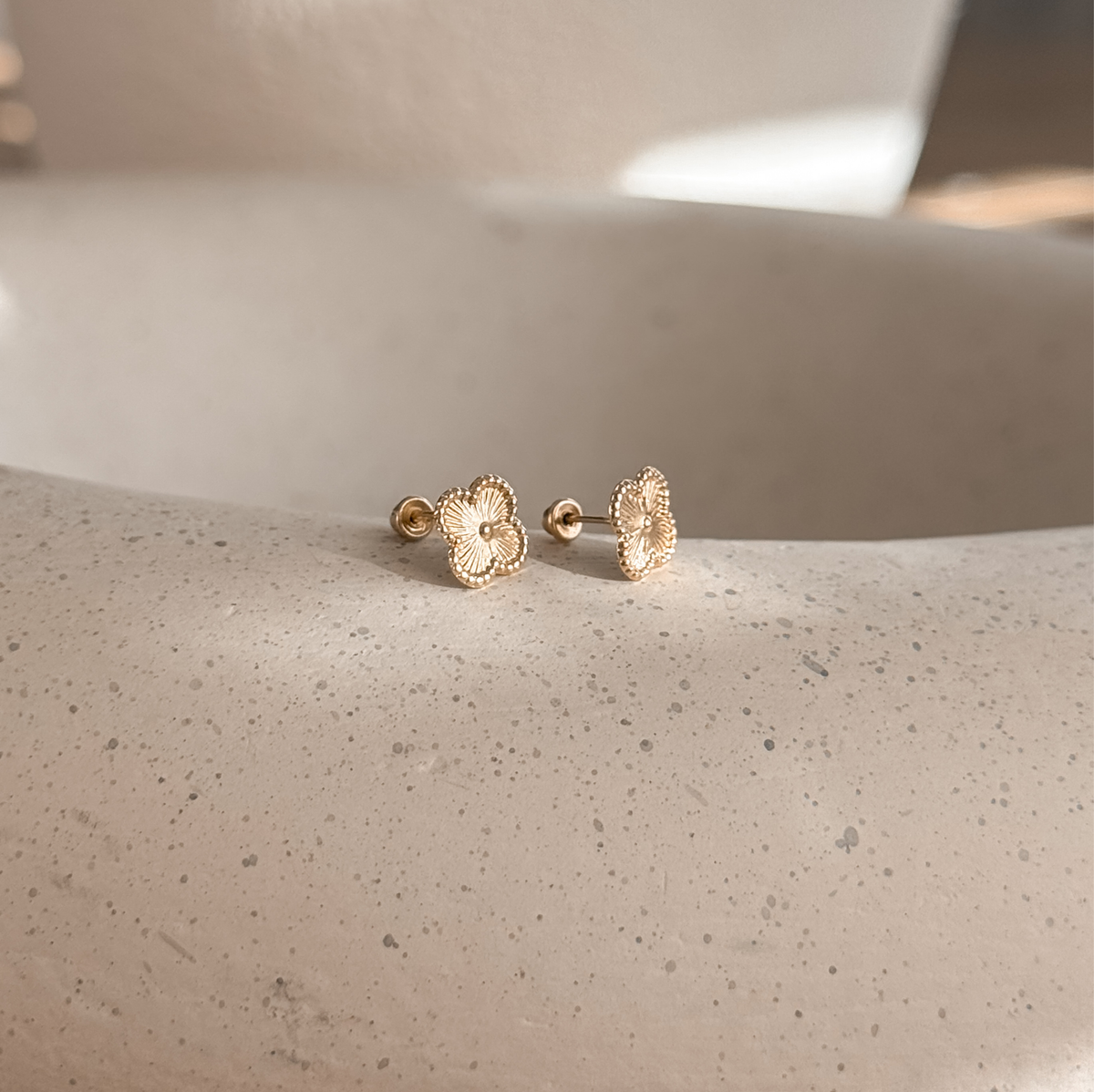 Solid gold clover flower studs with screw backs on a stone dish, side view – Liv Aura