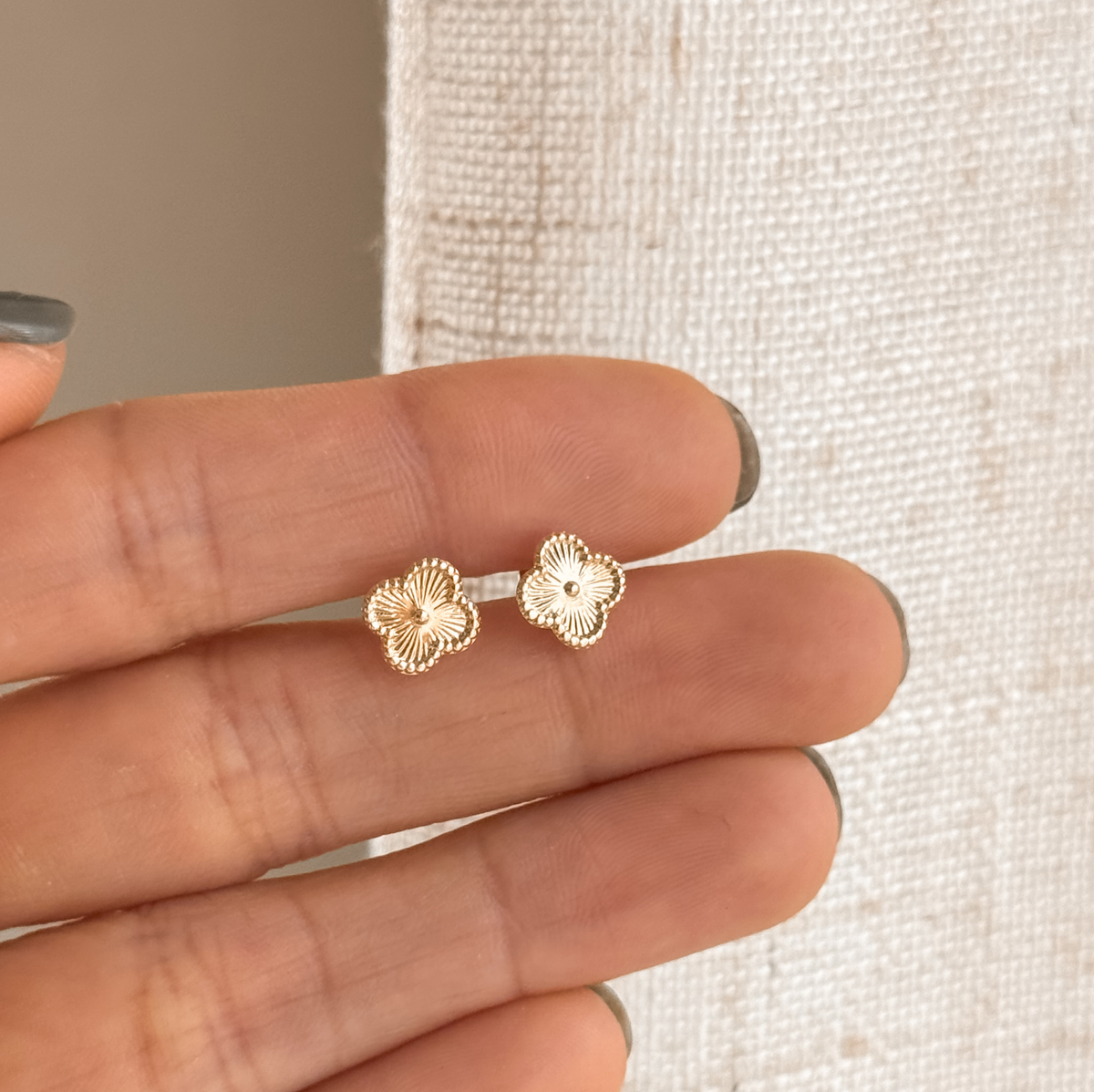 Solid gold clover flower stud earrings held in hand to show the size – Liv Aura