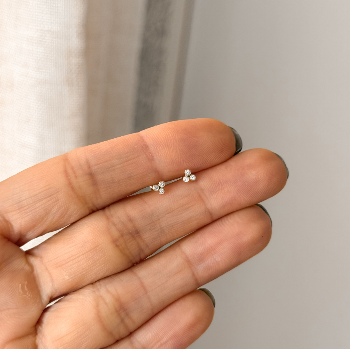 Tiny solid gold CZ trio bezel stud earrings held in hand to show the size – Liv Aura