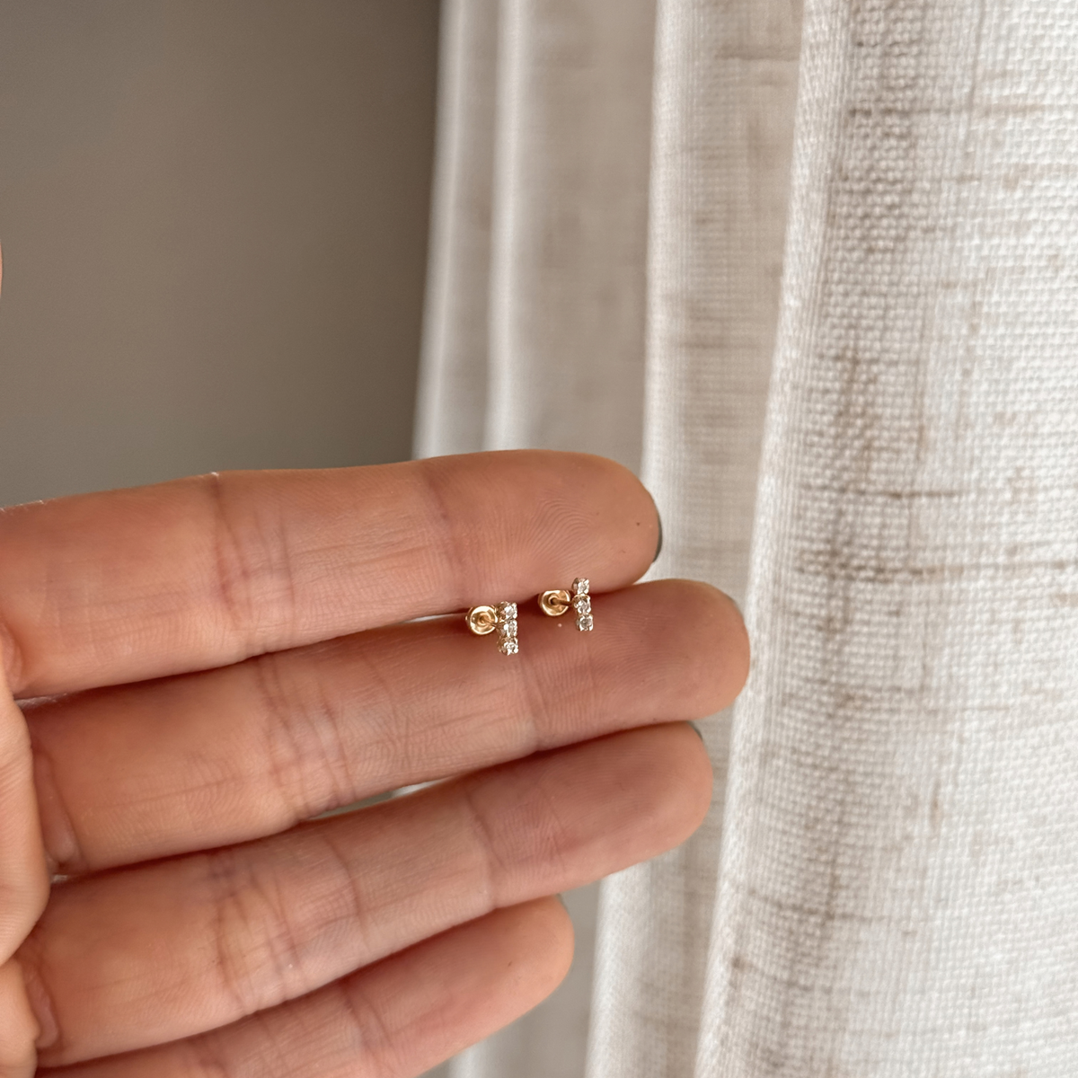 10K solid gold white CZ bar stud earrings held in hand to show the size – Liv Aura