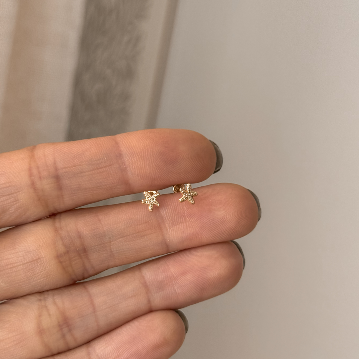 Tiny 10K solid gold starfish stud earrings held in hand to show the size – Liv Aura