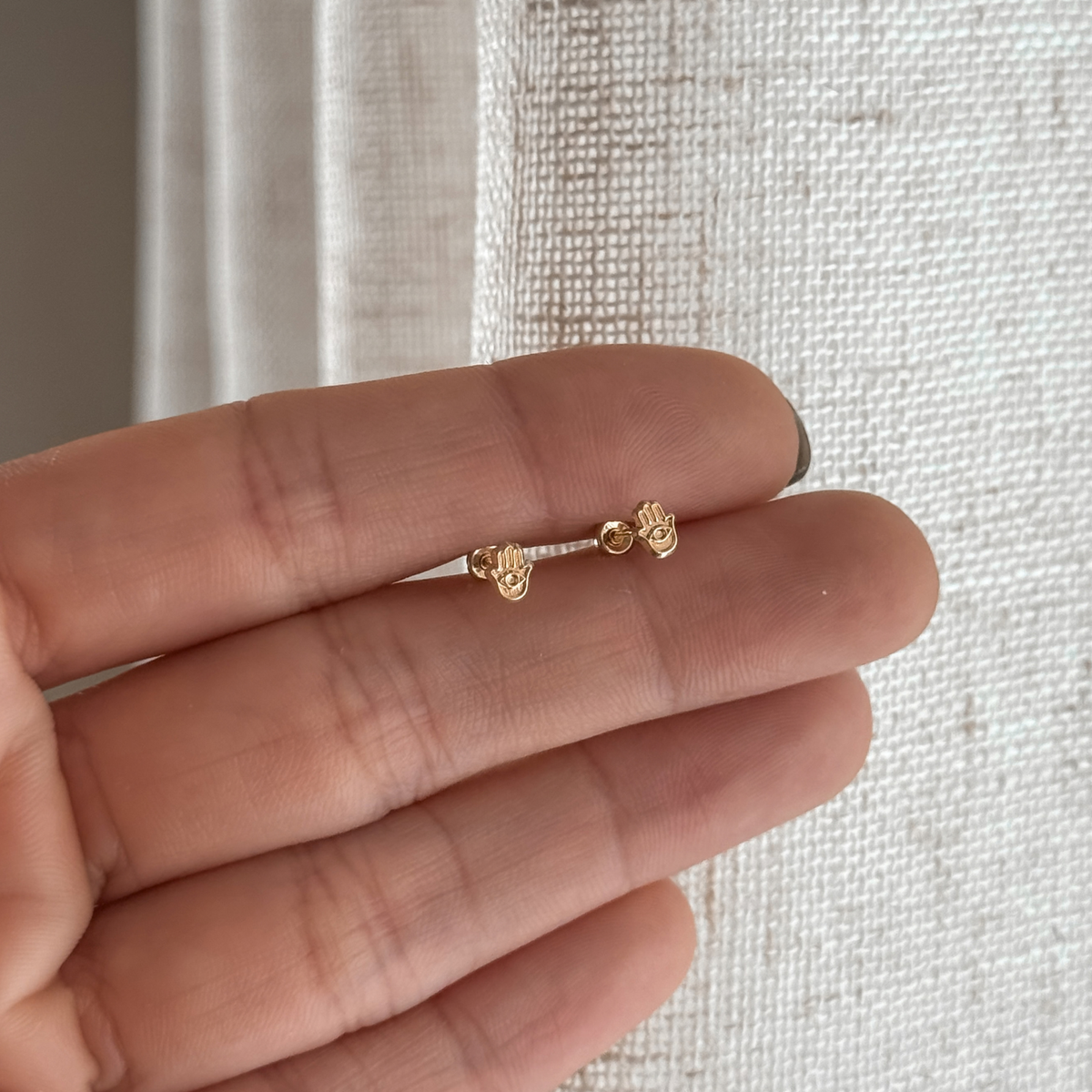 10K solid gold mini hamsa hand stud earrings held in hand to show the size – Liv Aura