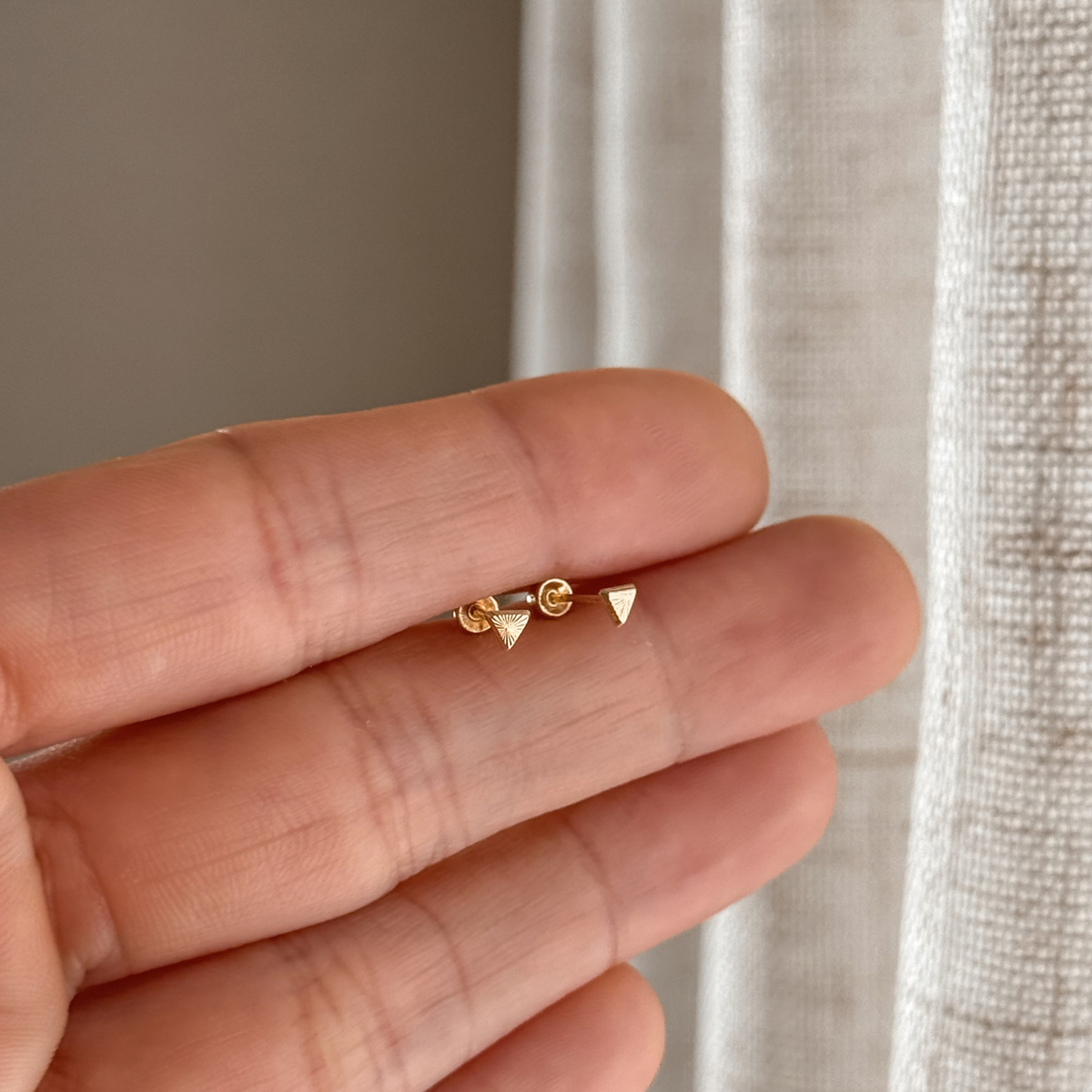 10K solid gold mini triangle stud earrings held in hand to show the size – Liv Aura