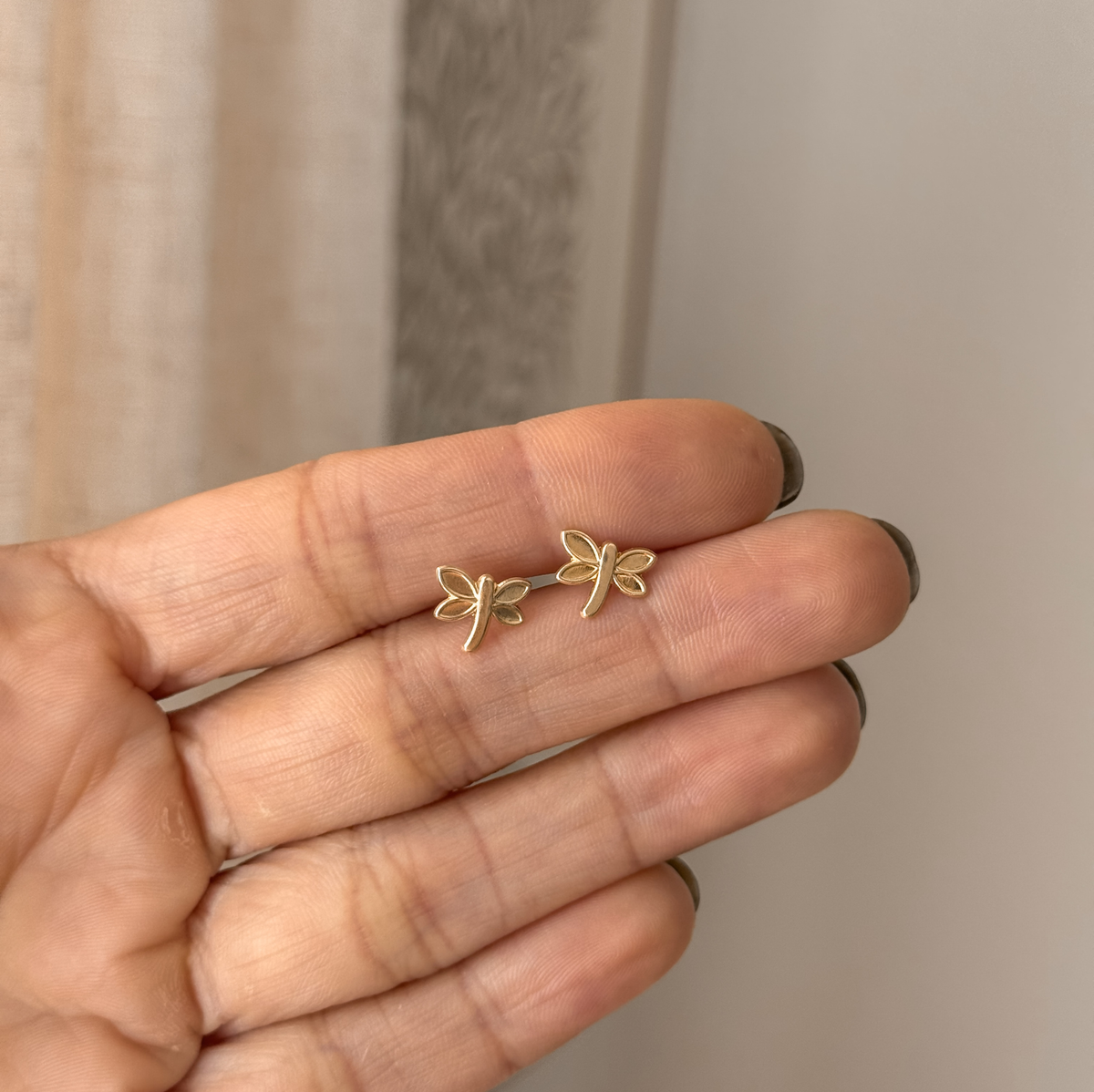 10K solid gold dragonfly stud earrings held in hand to show the size – Liv Aura