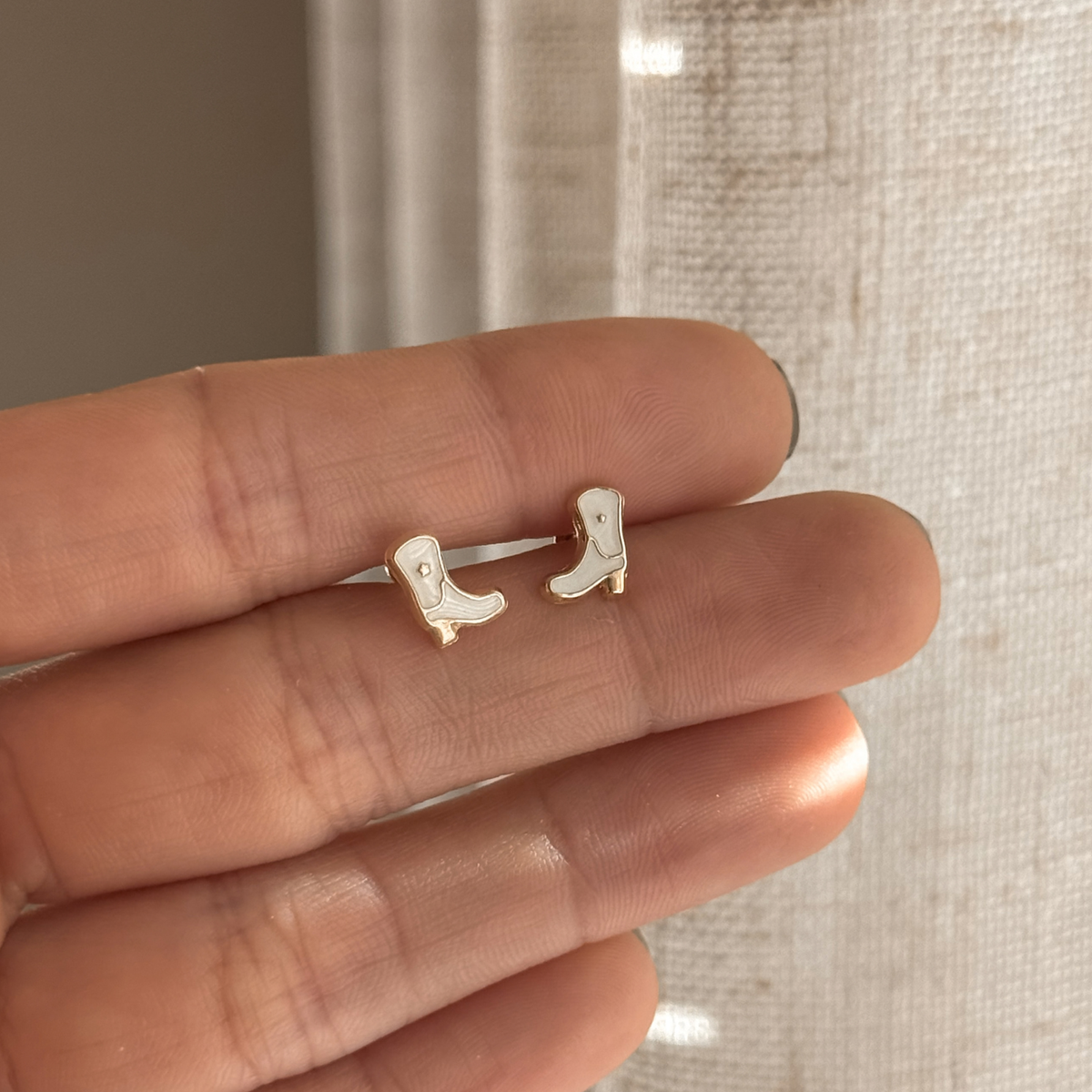 10K solid gold cowboy boot stud earrings with white enamel held in hand – Liv Aura