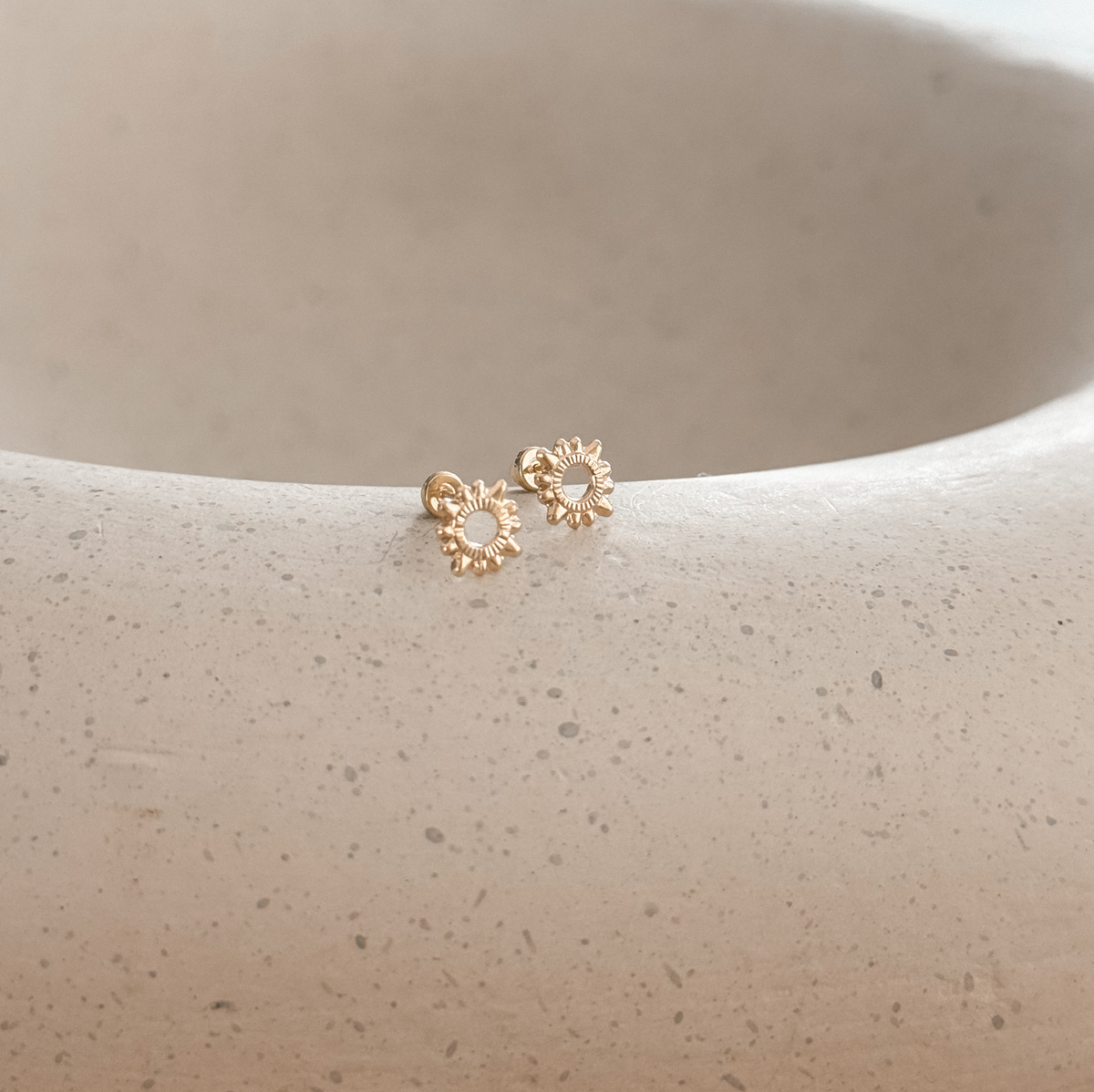 Pair of 10K solid gold sun studs with screw backs on a stone dish, close-up – Liv Aura