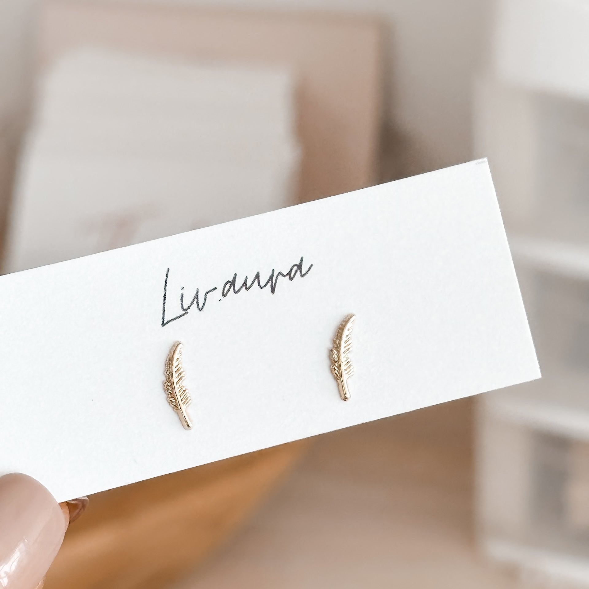 Feather stud earrings in 10K gold shown on silicone ear, highlighting their curved shape and minimalist style.